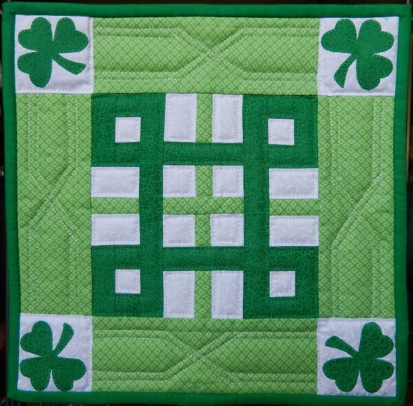 A green and white quilt with four leaf clovers.