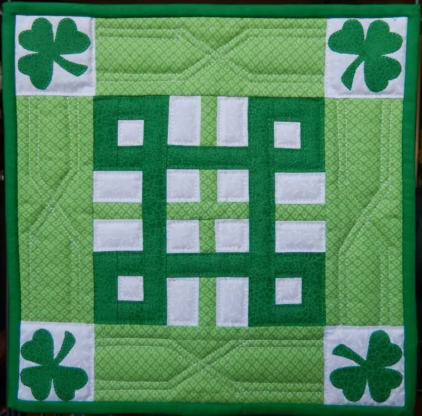 A green and white quilt with four leaf clovers.