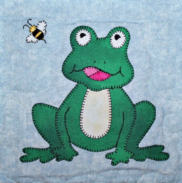 A frog and bee quilt with the frog sitting on it.