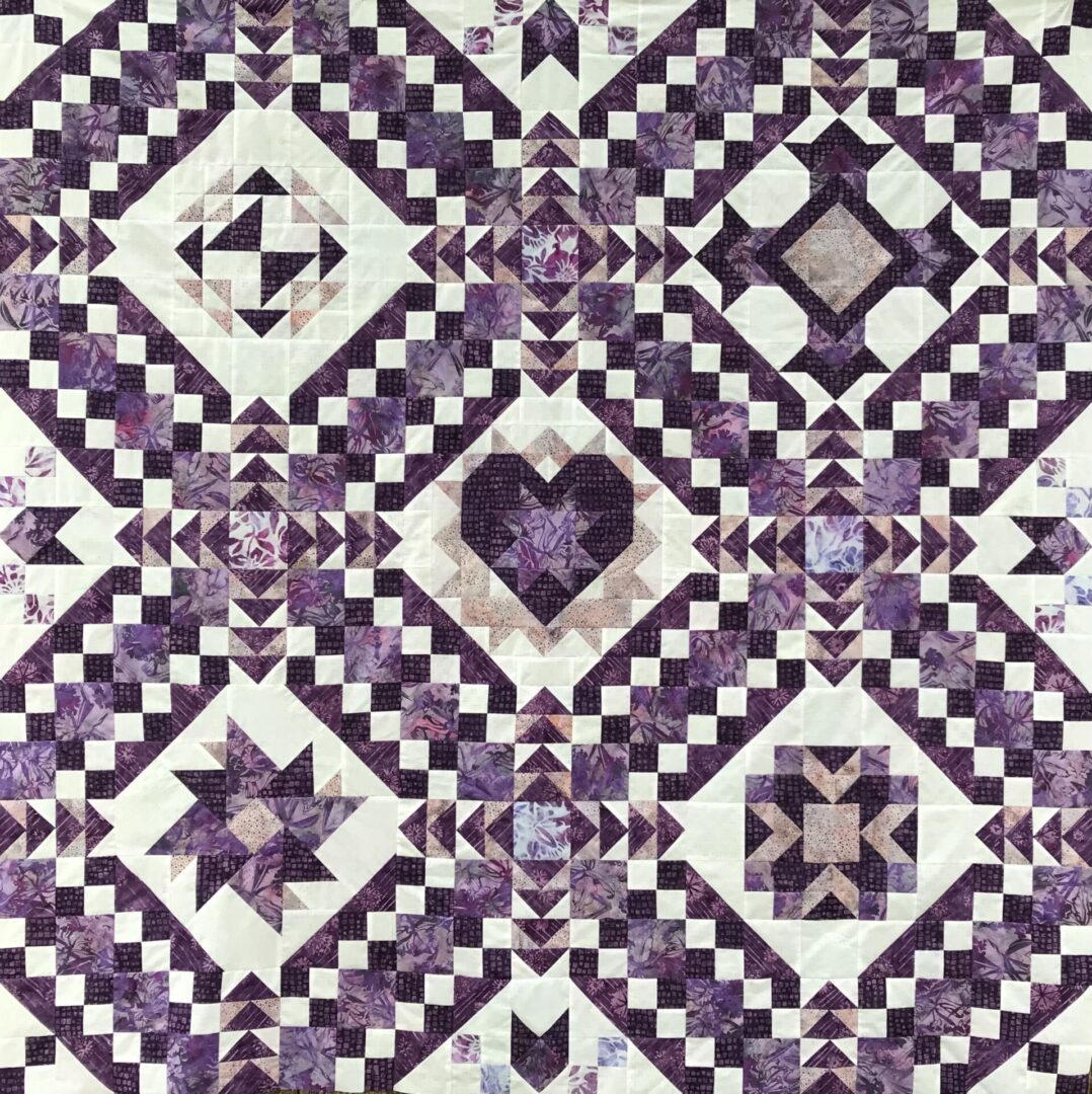 A quilt with different designs of purple and white.
