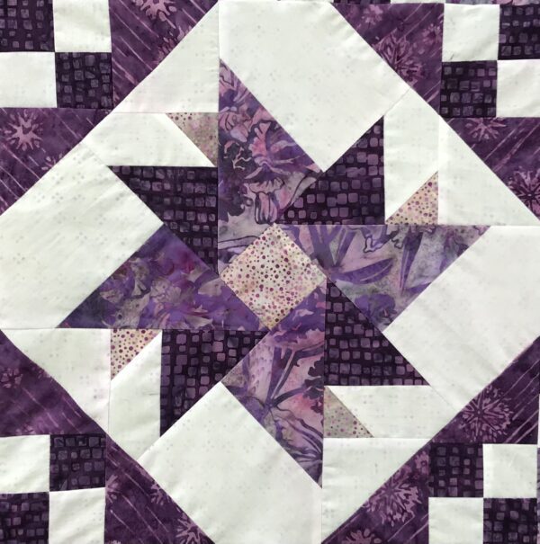 A quilt with purple and white designs on it.