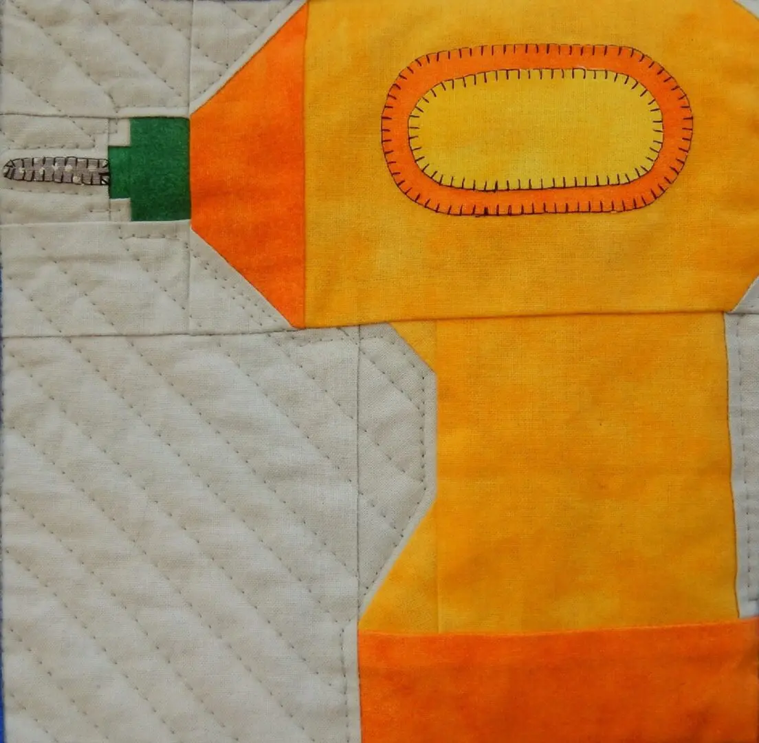 A yellow and orange quilt with an electric drill.