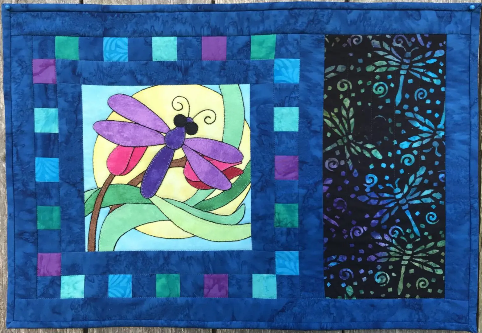 A colorful picture of a dragonfly on the front of a quilt.