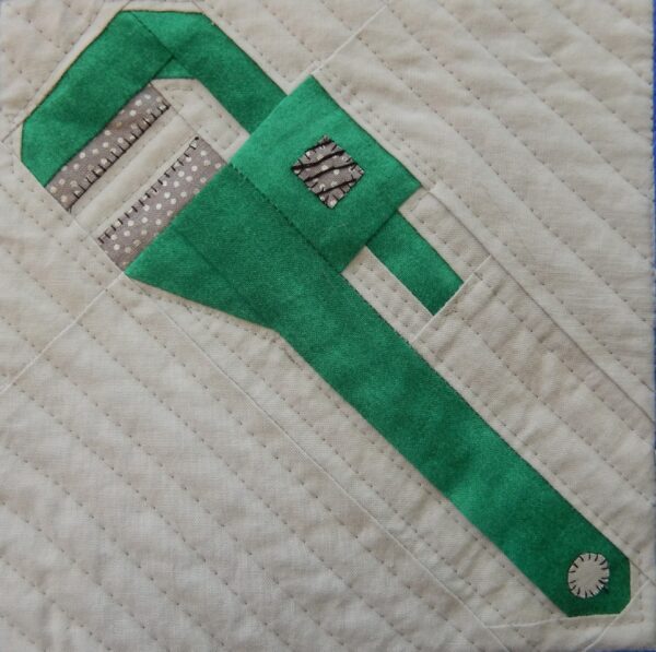 A green wrench is on top of the quilt.