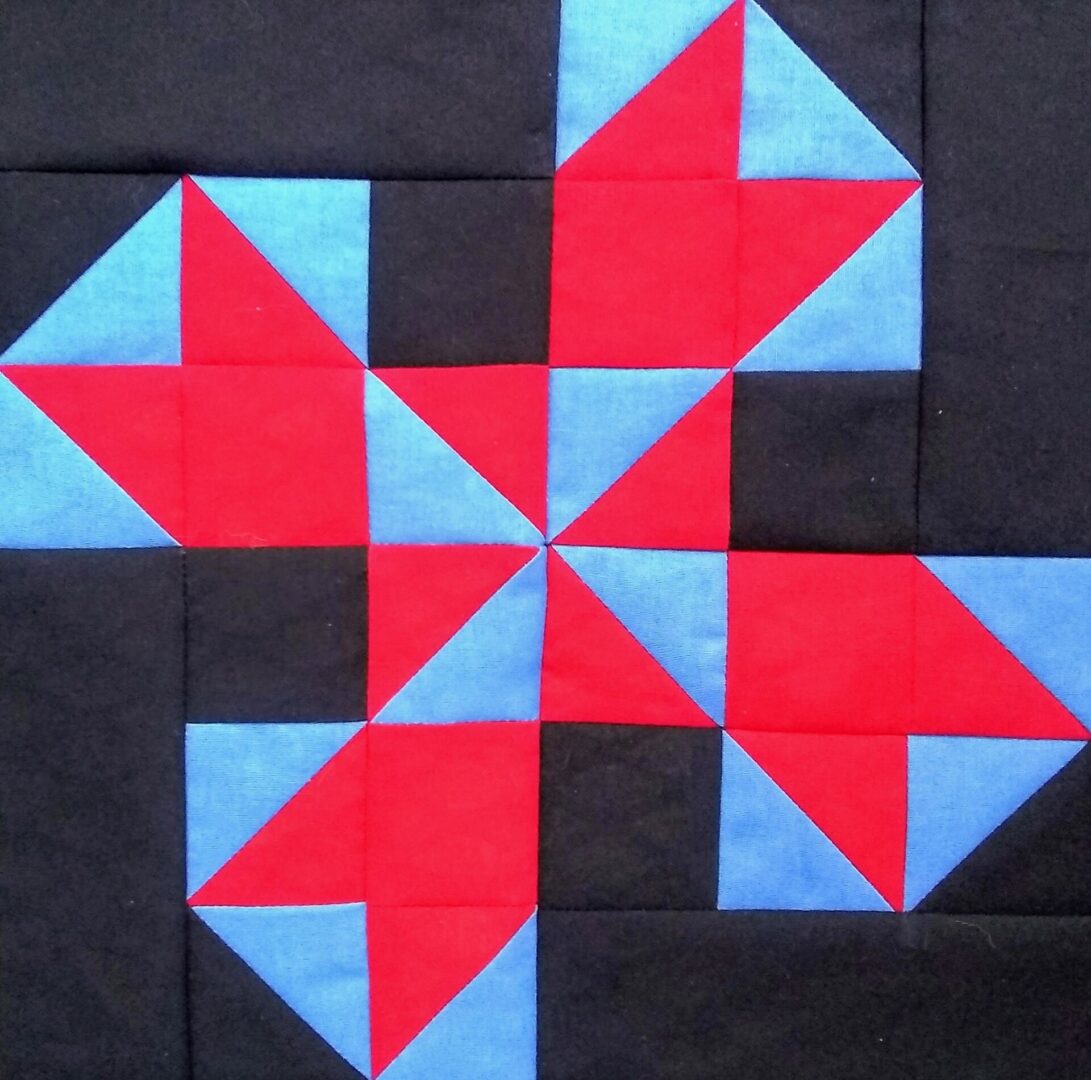 An Oklahoma Twister quilt block with red, blue and black squares.