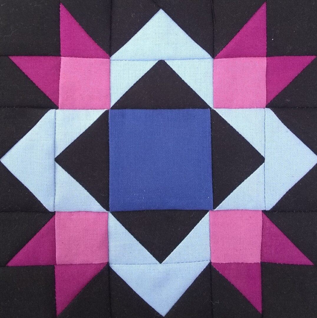 A close up of a Blueberry Pie - Small quilt block with blue and pink stars.