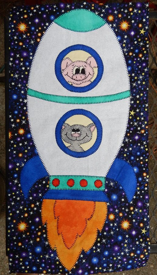 A quilt with a Space Race - Large Rocket and a teddy bear on it.