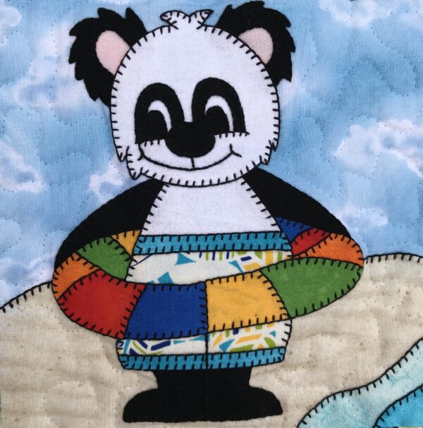 A Floaty Bear wearing a life preserver on a beach.