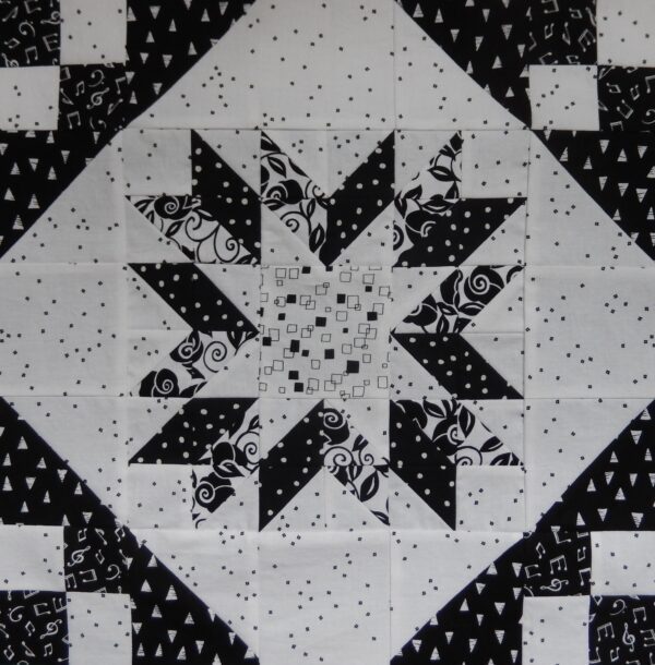 A black and white quilt block with a Fractured Star in the middle.