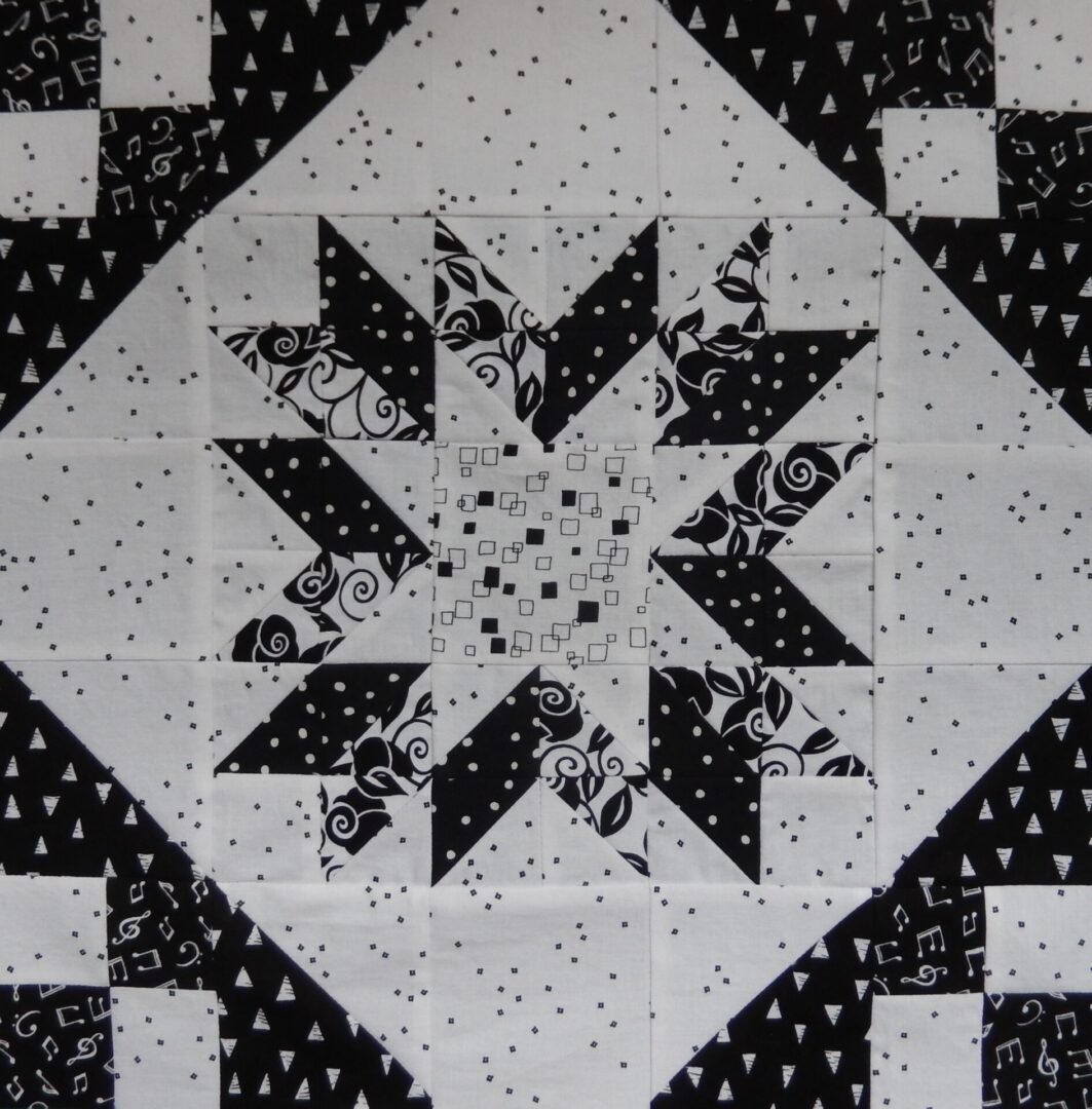 A black and white quilt block with a Fractured Star in the middle.