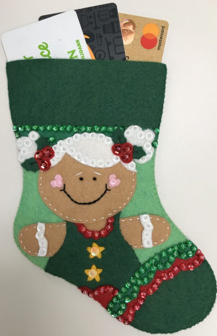 A Christmas stocking with a Gingerbread Girl A Gift Card Holder and credit cards.