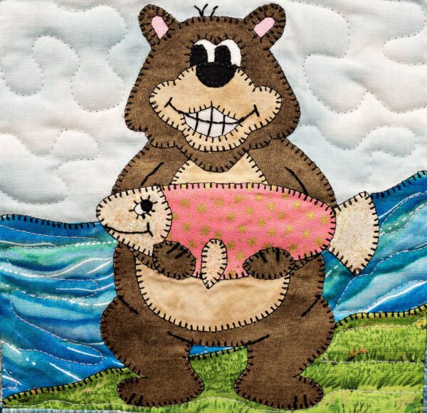 A Grizzly holding a fish on a quilted wall hanging.