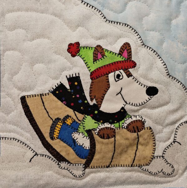 A Husky - Toboggan is riding a sled on a quilt.