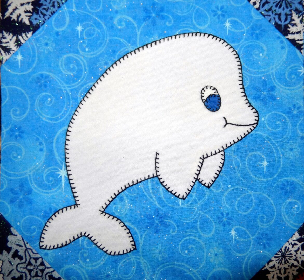 A blue quilt block with a Beluga Whale on it.