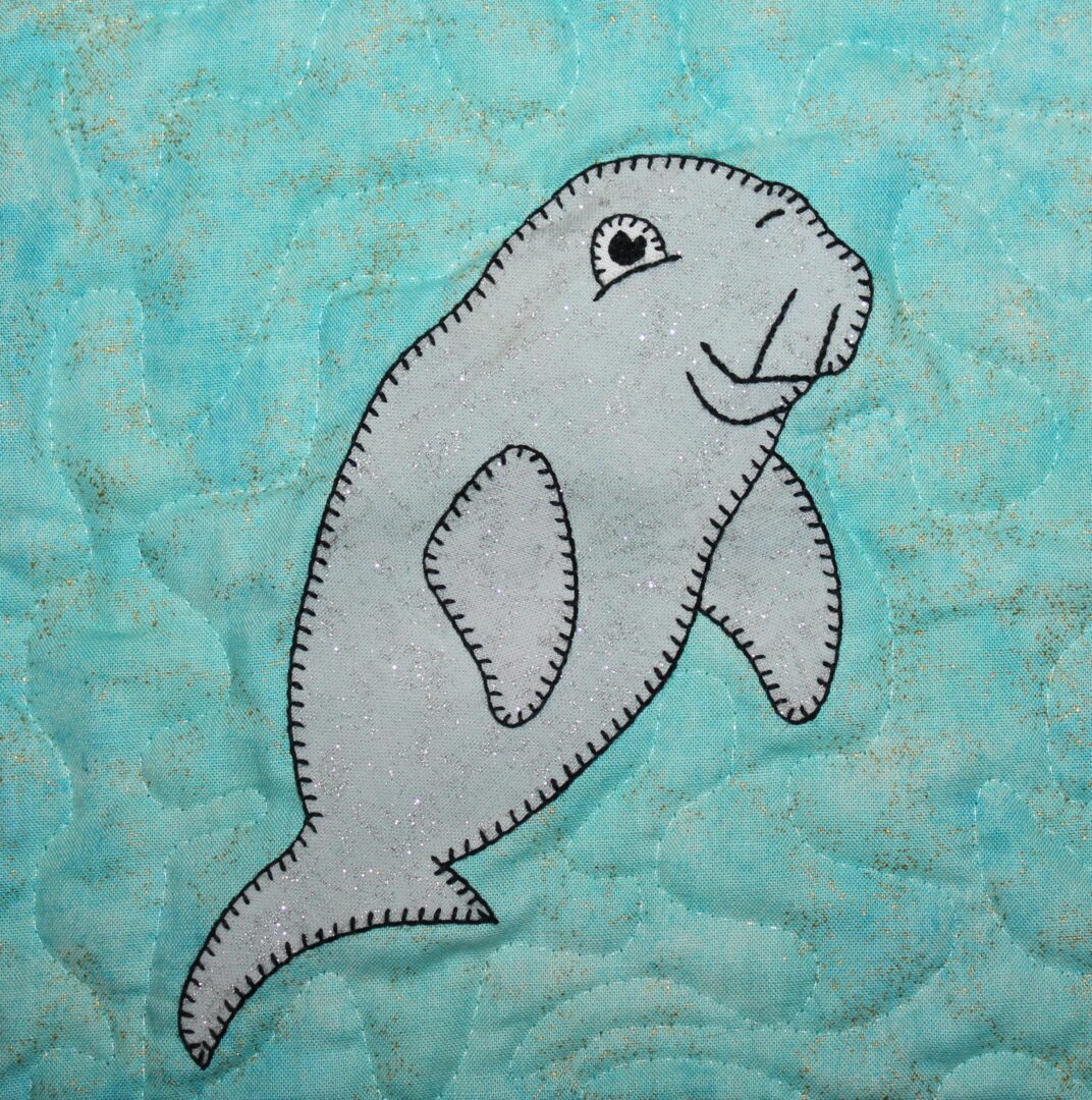 A dugong is appliqued on a blue quilt.