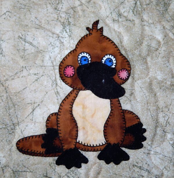 A Platypus stuffed animal with blue eyes sitting on a piece of fabric.