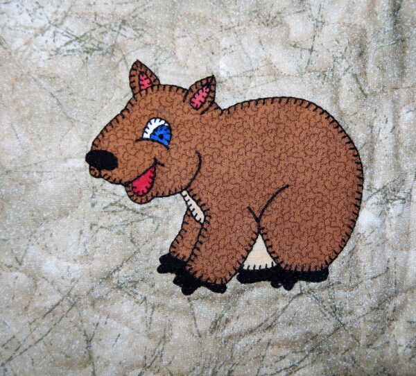 A brown bear with blue eyes is embroidered on a Wombat.